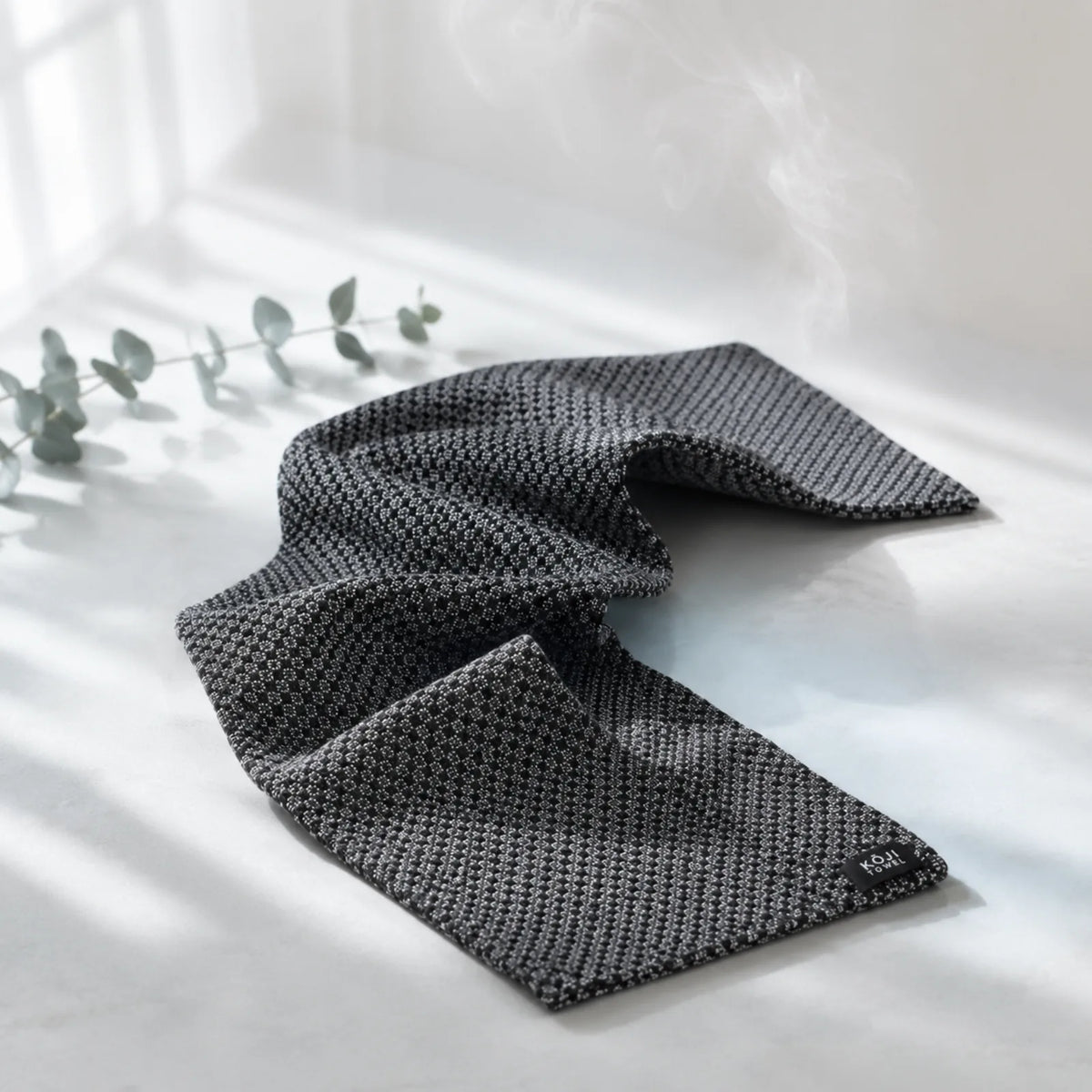 Exfoliační ručník Kōji Face Towel rozvlněný na světlém pozadí